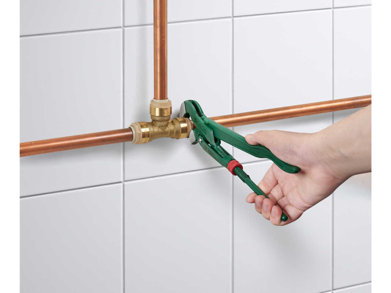 Chave de canalização Parkside apertando um tubo de cobre em azulejos brancos.
