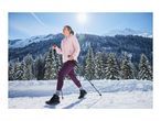 A woman in a pink jacket and purple leggings winter hiking with trekking poles.