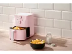 Roze friteza na vazduh sa pomfritom, činijom pomfrita i slanikom na drvenom pultu.