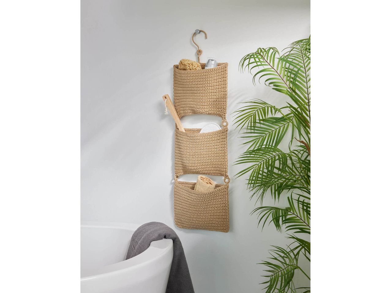 Cesto portaoggetti da bagno in macramè con spugne e spazzola, accanto a una vasca da bagno.
