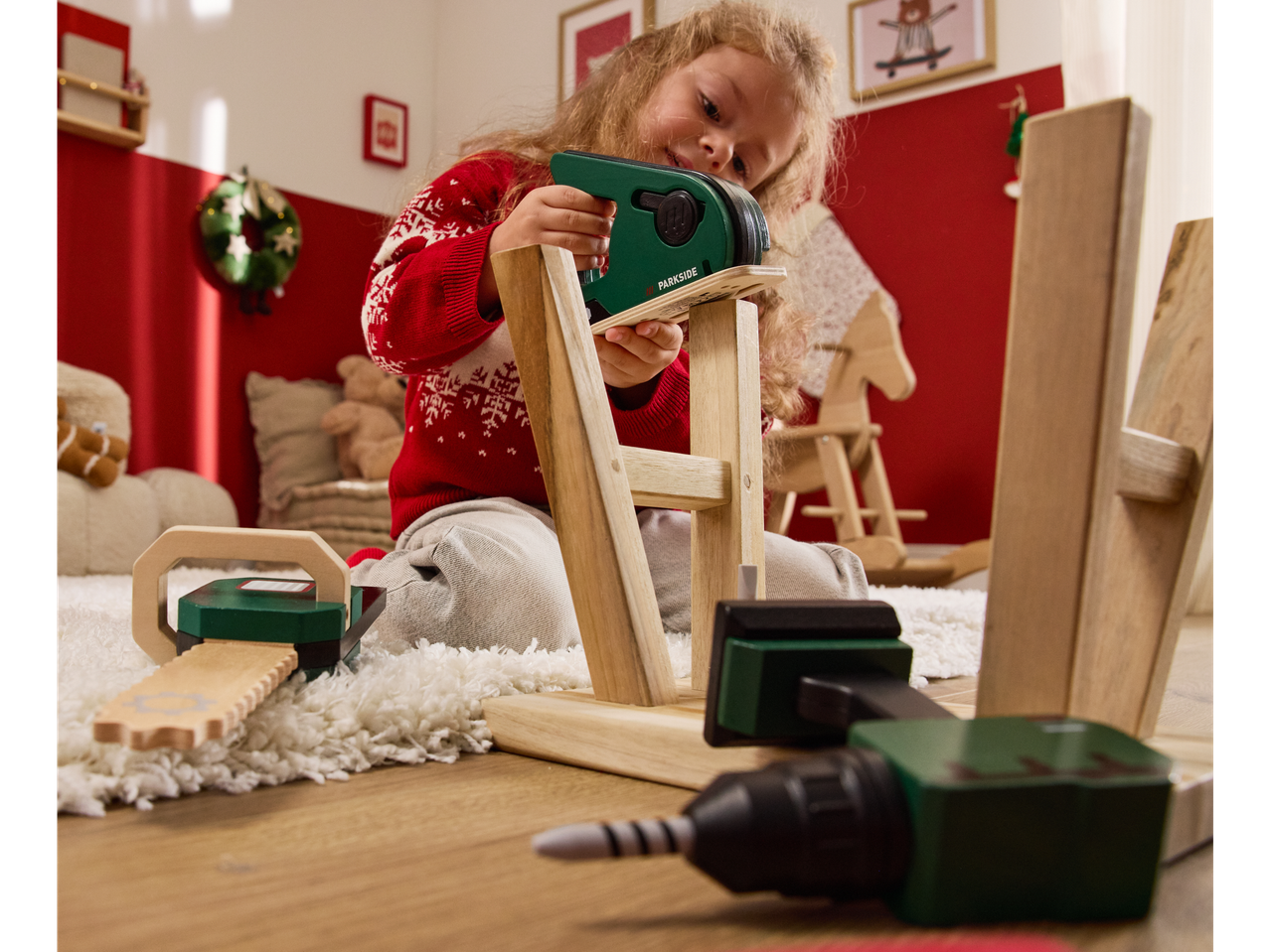 Devojčica se igra drvenim Parkside alatima, uključujući ubodnu testeru, motornu testeru i bušilicu.