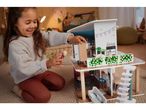A smiling girl playing with a wooden dollhouse and a doll.