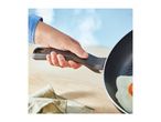 Hand holding a frying pan with a fried egg, on a wooden surface with a cloth.