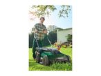 Man mowing a sunny lawn with a green lawnmower.