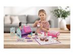 Young girl playing with a toy cash register, tea set, and play food on a wooden table.