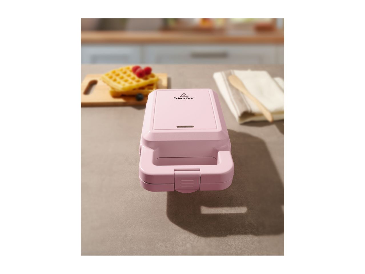 Pink SilverCrest waffle maker on a kitchen counter with waffles.