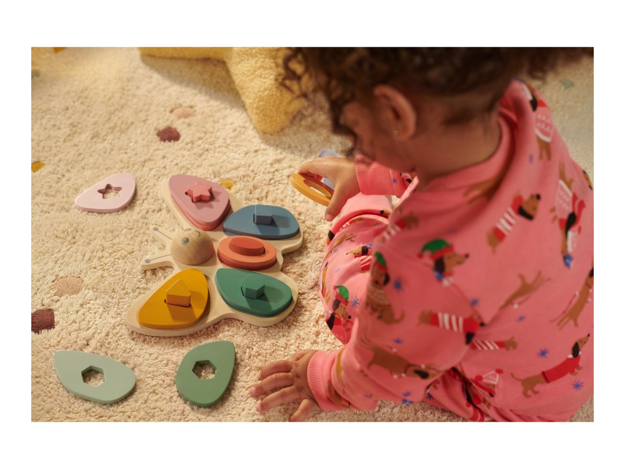 Child playing with a wooden butterfly shape sorter on a cream rug.