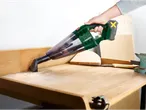 Uma pessoa usa um aspirador de pó manual sem fio Parkside para limpar serragem de uma bancada de madeira.