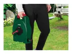 Person holding a green hose reel with a red handle in a garden setting.