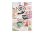 Pink espresso machine with a cup of coffee and desserts on a counter.