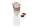 Double-walled glass holds a layered latte; two macarons sit beside it.