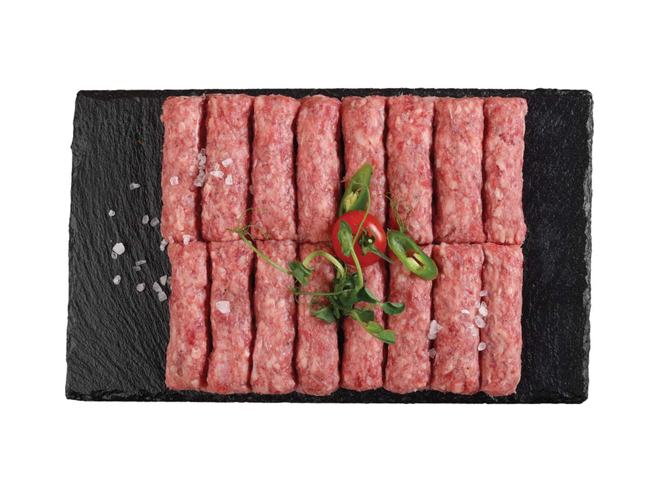 Sveži ćevapi na crnoj ploči sa solju, paradajzom i zelenim papričicama.