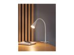 A white clip-on desk lamp illuminates a notebook and pen on a wooden desk.