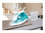 Steam iron on an ironing board with a measuring cup of water, clothes in the background.