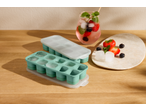 Formas de gelo verde menta com tampas, bebida de frutas e bagas numa mesa de madeira.