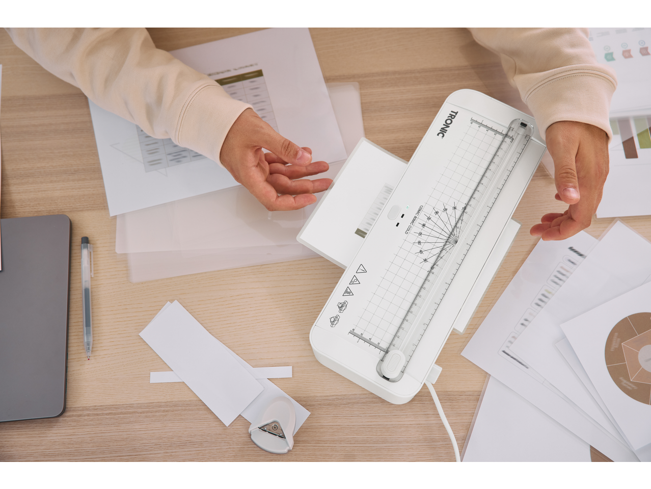 Laminador TRONIC sobre a mesa, mãos a colocar um documento para laminar.