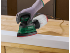 Lixadeira Parkside com mão enluvada, lixando uma tábua de madeira branca.