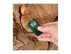 Hand holding a wood moisture meter showing 20.0% moisture and 28°C, against a background of cut logs.