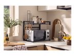Microwave oven on a black metal shelf with kitchen utensils, jars, and cutting boards.