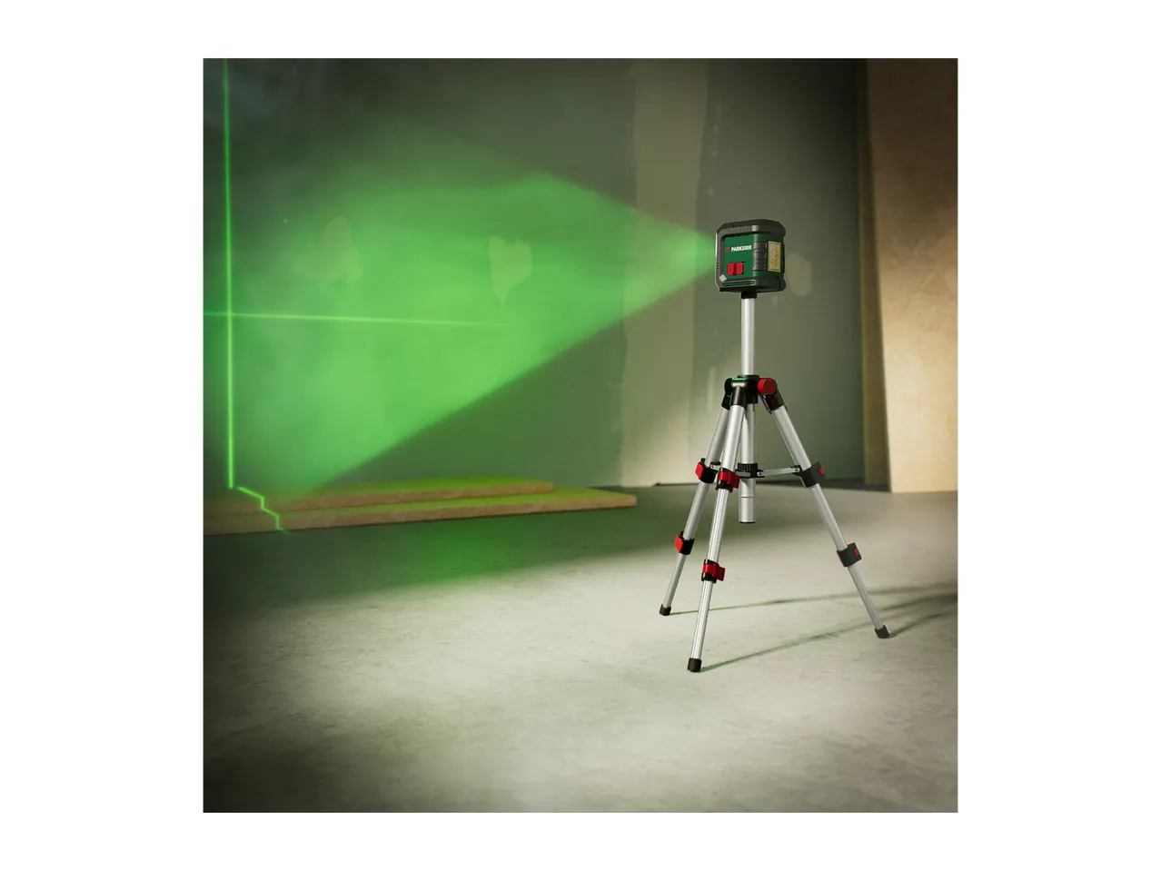 A green laser level on a tripod projects lines onto a wall in a room under construction.