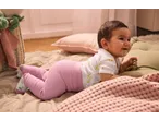 Happy baby in a white bodysuit with giraffes and pink ribbed leggings, playing on a soft mat.