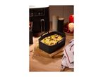 Air fryer with a baking dish of gratin, surrounded by festive candles and spices.
