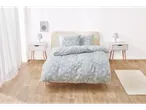 Set de lenjerie de pat cu model de frunze albastru deschis, pe un pat într-o cameră luminoasă.