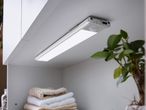 LED under-cabinet light with motion sensor, illuminating stacked towels in a cabinet