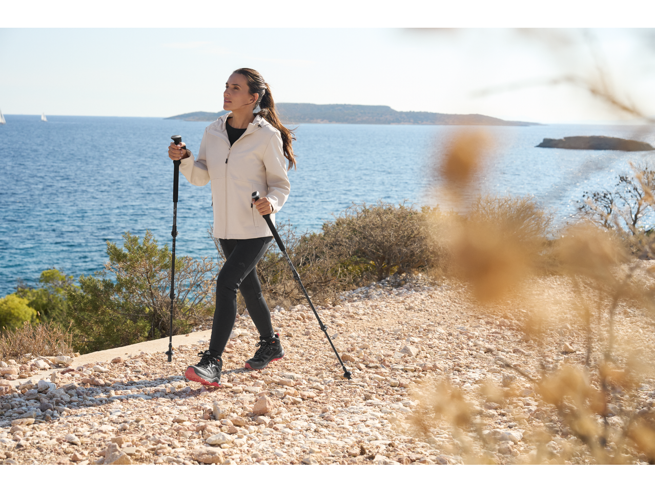 Woman in a light jacket and dark leggings nordic walking by the sea.