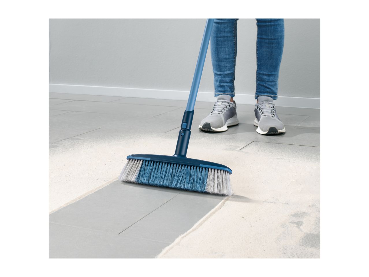A person sweeps a floor with a long-handled brush.