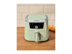 Light green air fryer on a wooden counter with a plate of fries beside it.