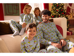 Family wearing matching Grinch Christmas pajamas, sitting on a sofa in a festive living room.