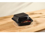 Black roasting pan with lid, filled with chopped fruit, on a woven mat on a wooden surface.