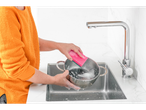 A woman washes a pot with a sponge in the sink.