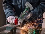 Person in workwear and gloves using an angle grinder to cut metal, creating sparks.