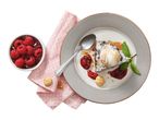 Chocolate brownie with ice cream, raspberry sauce, and mint on a plate with a bowl of raspberries.