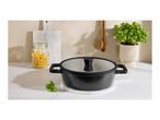 Black cooking pot with glass lid on a marble trivet, with pasta, basil, and wooden utensils.