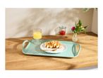 Breakfast tray with waffles, orange juice, jam, and flowers on a wooden counter.