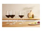 Red wine glasses on a wooden counter with cheese and grapes.