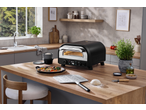 Forno de pizza SILVERCREST e placa de ferro fundido com pizza numa bancada de cozinha de madeira.
