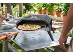 Cuptor de pizza exterior cu o pizza proaspăt coaptă pe o lopată, gata de servit la o petrecere în grădină.