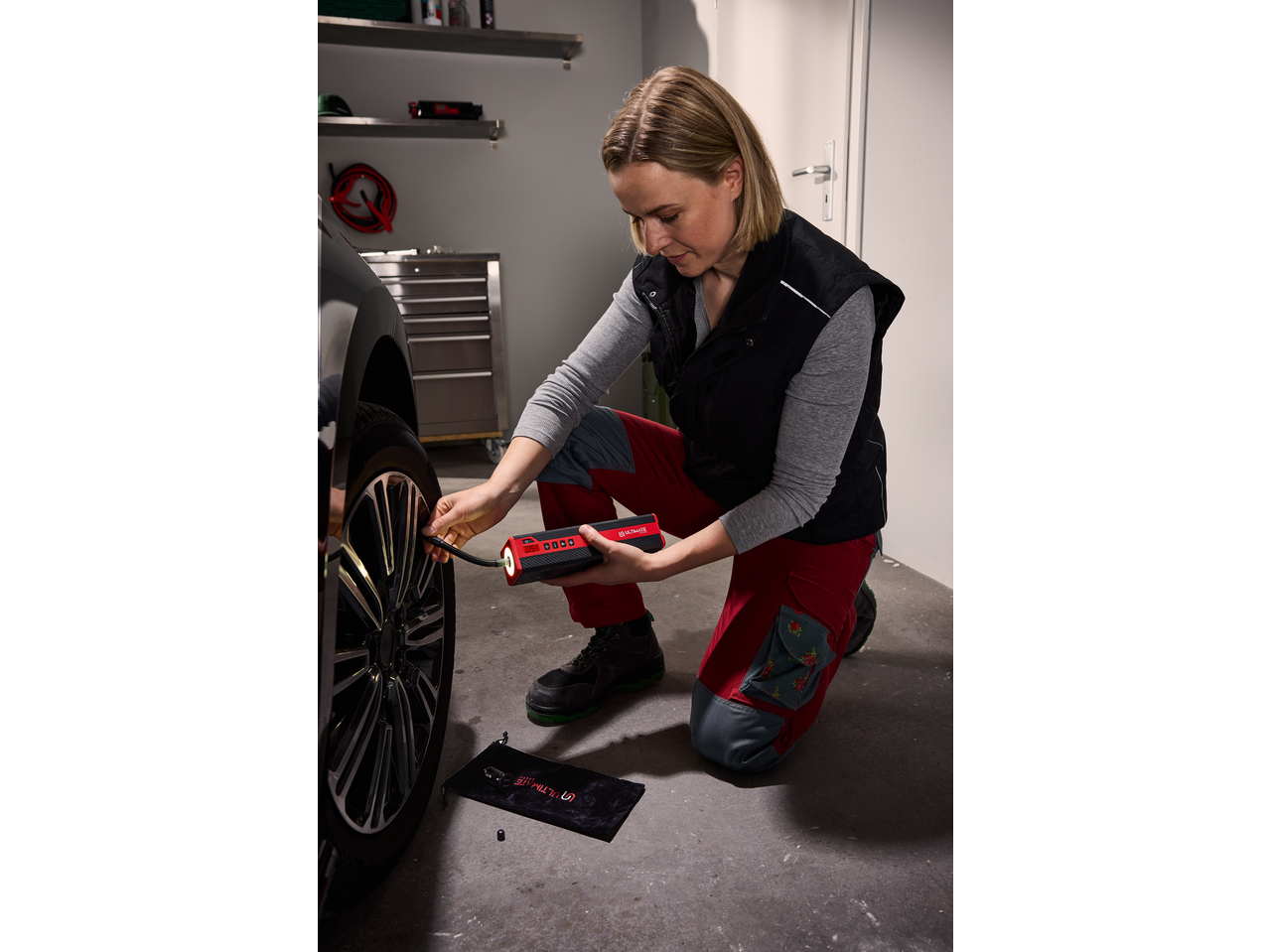 Woman inflating car tire with a portable air compressor in a garage.