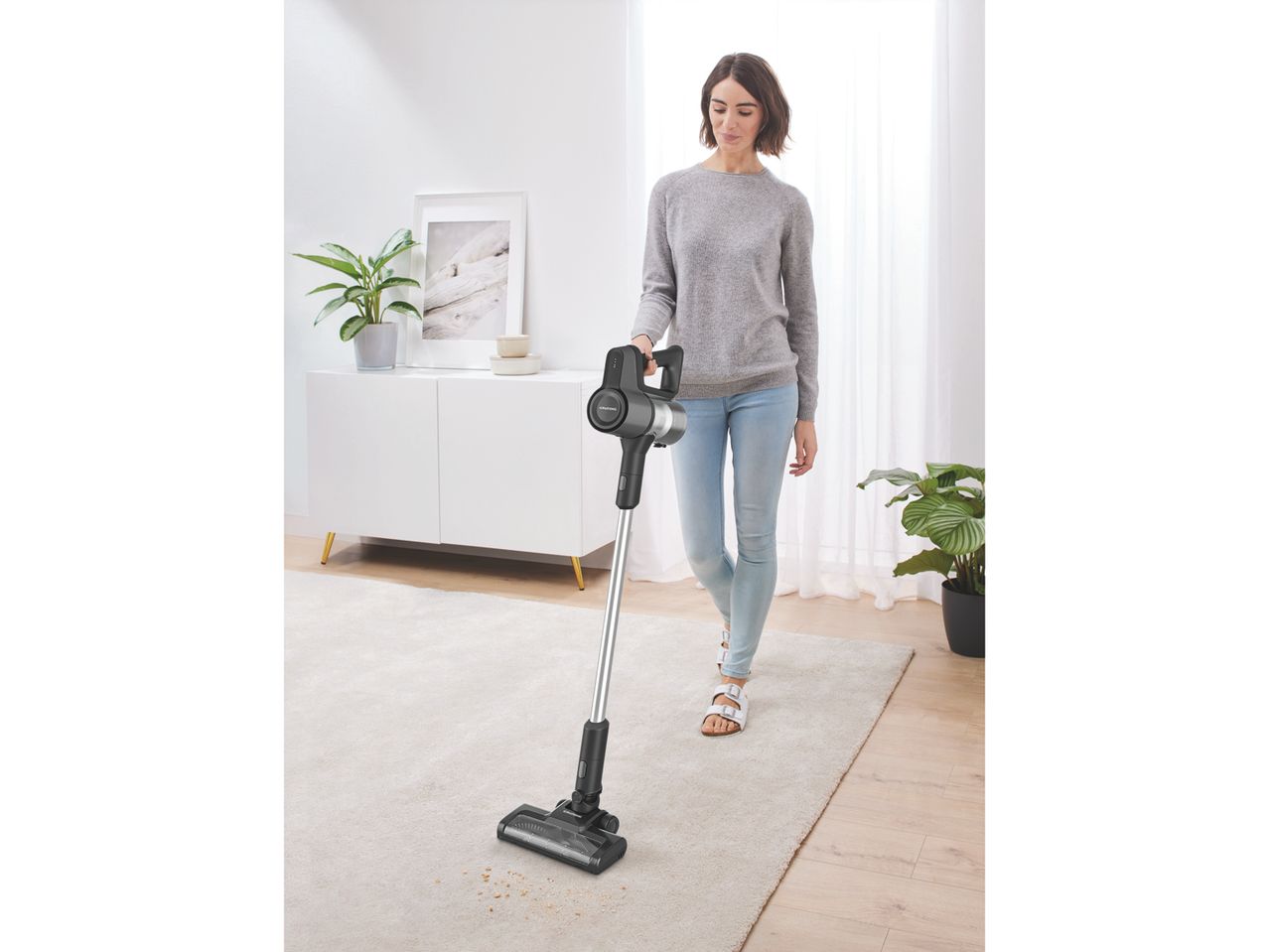 Una donna aspira lo sporco da un tappeto con un aspirapolvere a bastone Grundig.