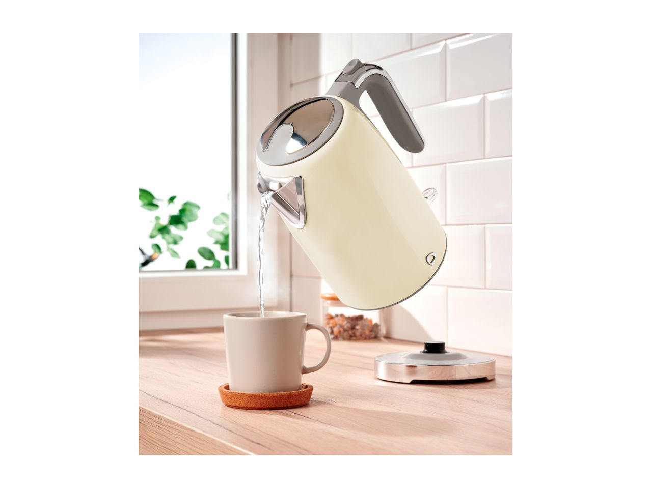 An electric kettle pouring hot water into a mug on a kitchen counter