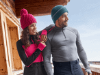 Ein Paar in Winterkleidung, die Frau trägt eine pinke Mütze und der Mann eine blaue Mütze, auf einem Balkon.