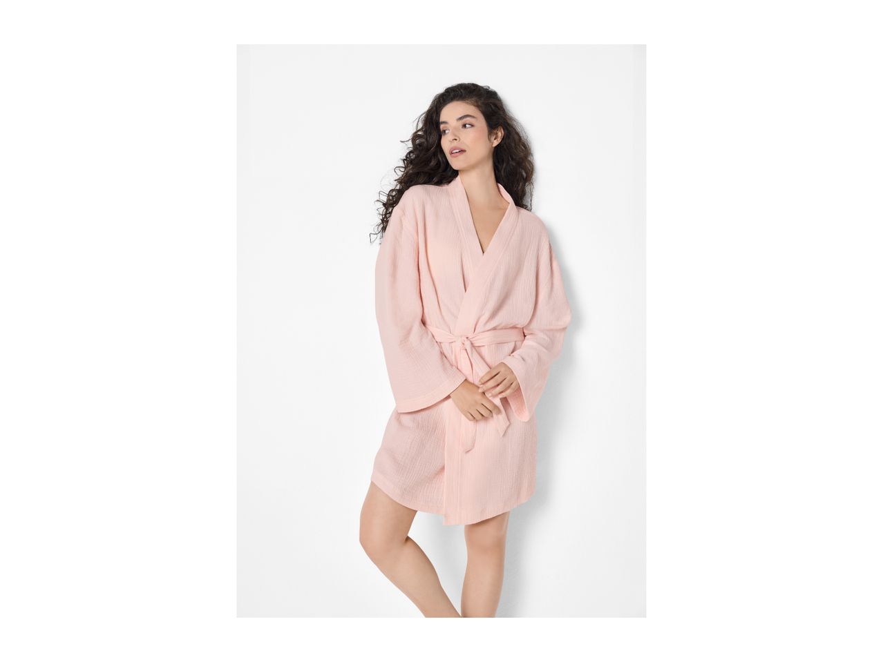 Woman with dark curly hair wearing a light pink short bathrobe