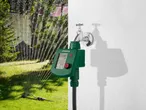 Kerti öntözőóra csapra szerelve, háttérben locsolóval öntözött zöld gyep.