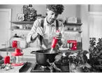 Man cooking with a red Silvercrest immersion blender, surrounded by red kitchen appliances.
