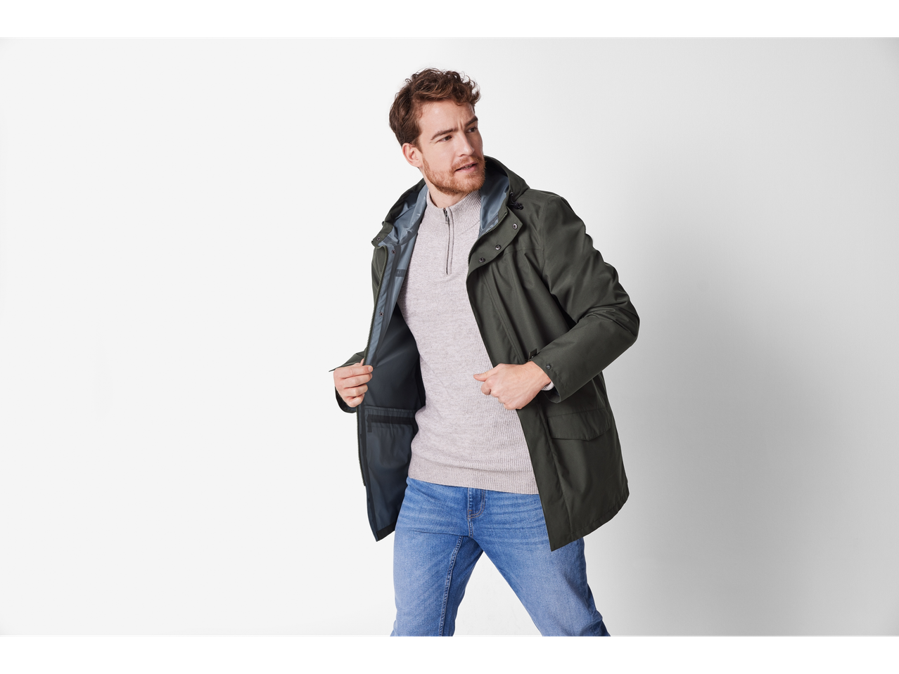A man in a dark green jacket, light grey sweater, and blue jeans.