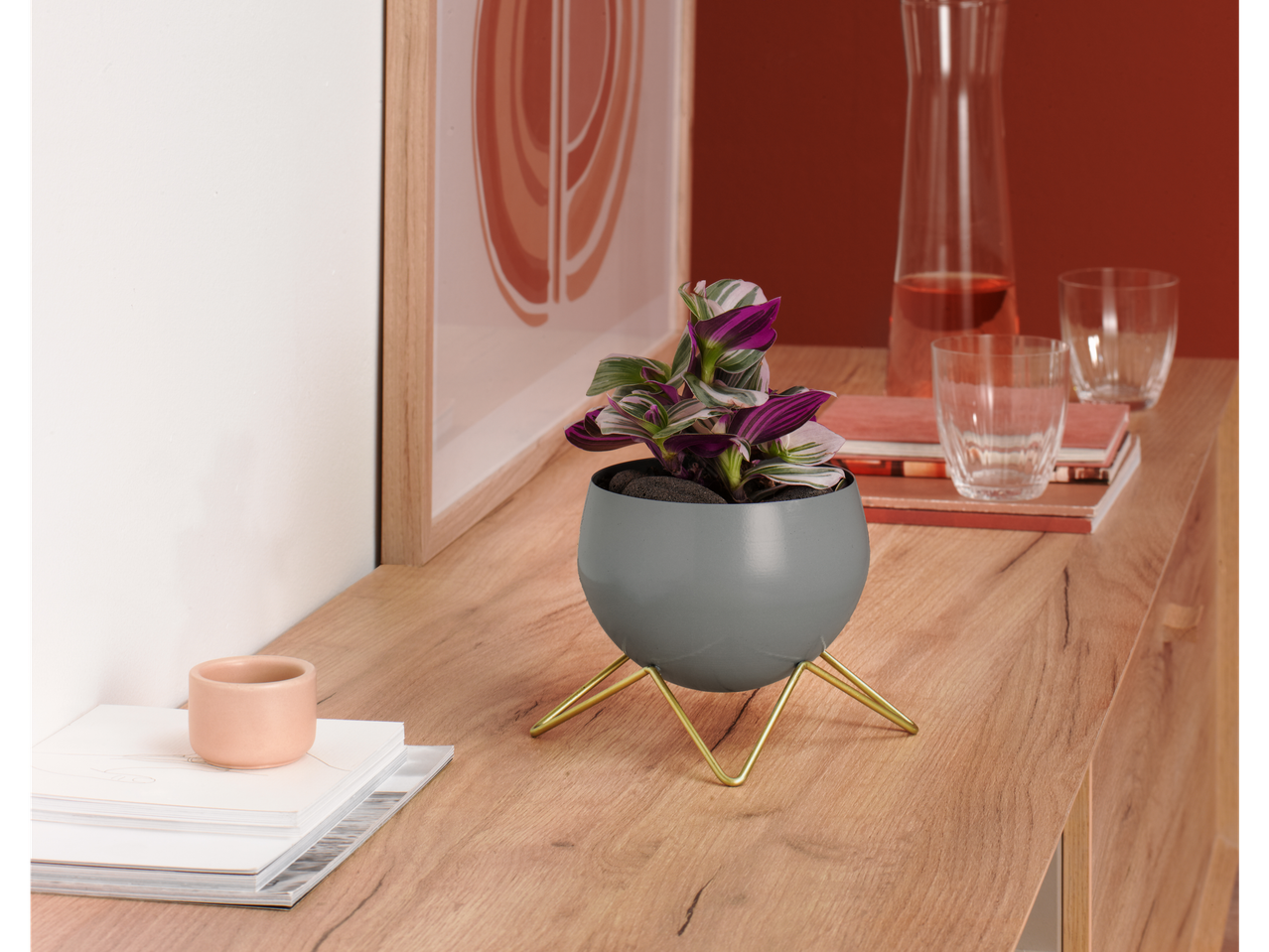 Vaso de flores cinza com uma planta roxa em uma mesa de madeira.